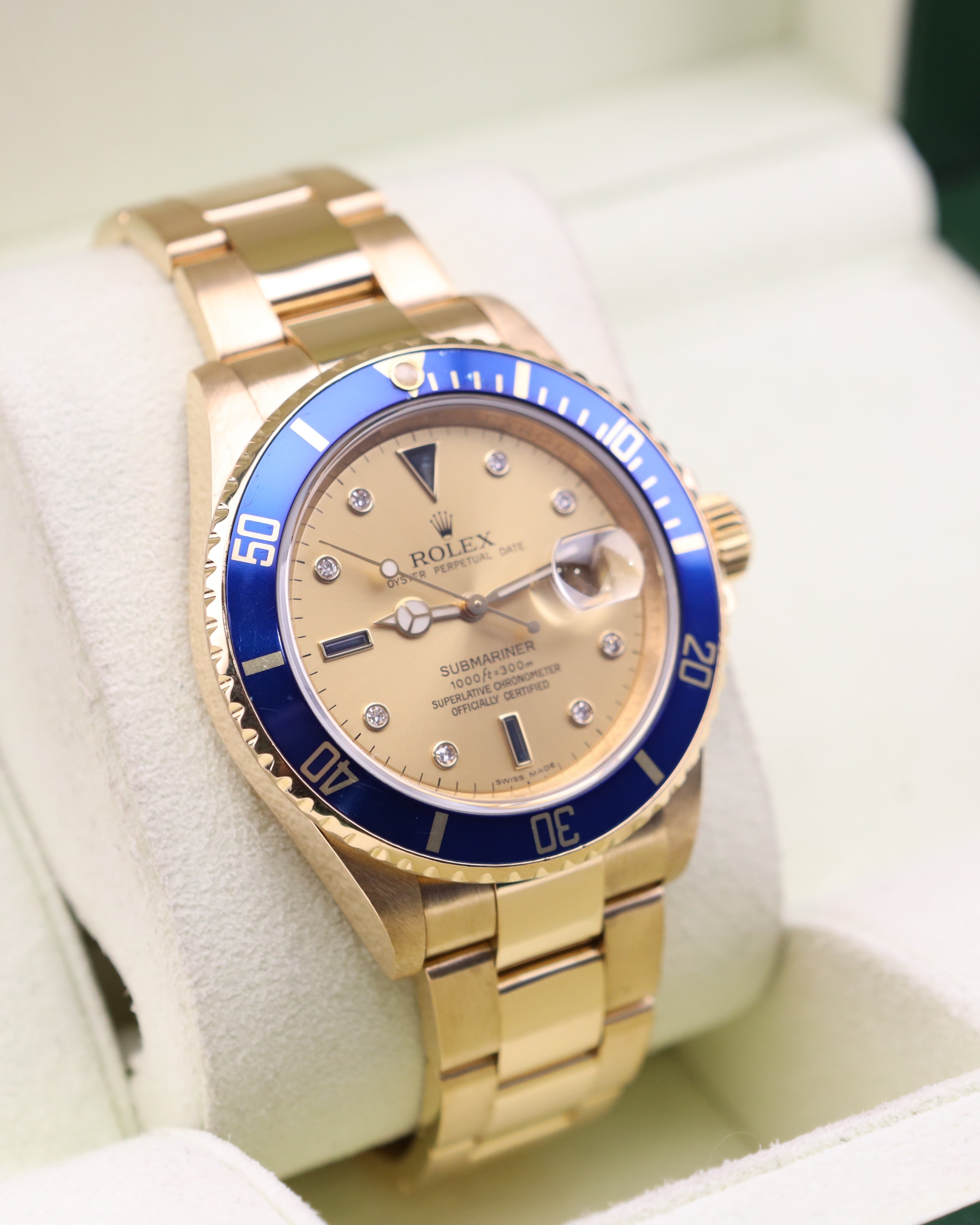 Gold watch with blue bezel and beige face on a white background